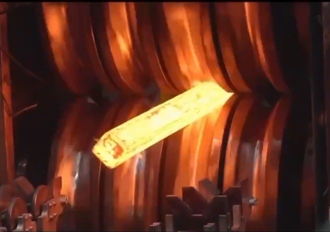 Heated metal billet being shaped by roll forging machine, showcasing precision forming process